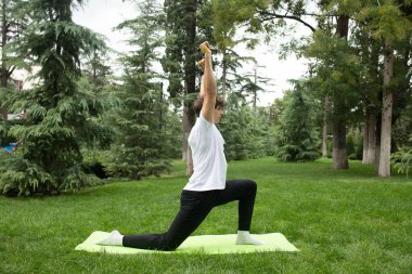 Güneşli bir sabahta parkta yoga yapan bir adam. Açık havada yoga minderinde egzersiz yapan sağlıklı ve aktif yaşam tarzı kavramı olan zinde bir genç. Açık havada eğitim..