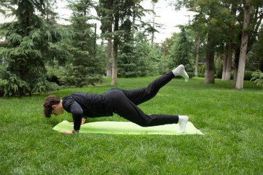 Güneşli bir sabahta parkta yoga yapan bir adam. Açık havada yoga minderinde egzersiz yapan sağlıklı ve aktif yaşam tarzı kavramı olan zinde bir genç. Açık havada eğitim..