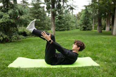 Güneşli bir sabahta parkta yoga yapan bir adam. Açık havada yoga minderinde egzersiz yapan sağlıklı ve aktif yaşam tarzı kavramı olan zinde bir genç. Açık havada eğitim..