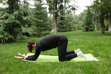 Güneşli bir sabahta parkta yoga yapan bir adam. Açık havada yoga minderinde egzersiz yapan sağlıklı ve aktif yaşam tarzı kavramı olan zinde bir genç. Açık havada eğitim..
