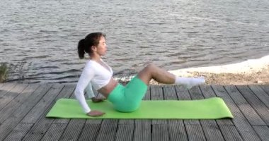 Göl kenarında egzersiz yaparken spor minderinde abdominal egzersizler yapan genç bir kızın portresi. Sağlıklı yaşam tarzı kavramı.