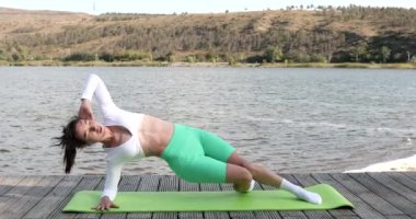 Göl kenarında egzersiz yaparken spor minderinde abdominal egzersizler yapan genç bir kızın portresi. Sağlıklı yaşam tarzı kavramı.