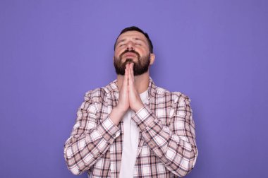 Mor arka planda izole edilmiş genç sakallı beyaz adam dua etmek için el ele tutuşuyor.     