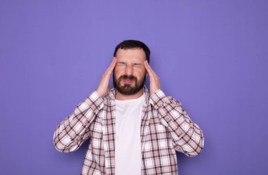 Mor arka planda migrenden muzdarip bir adam. Başında baş ağrısı olan sakallı yakışıklı bir adam..       