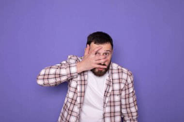 Mor arka planda, sakallı ve günlük giysileri olan genç beyaz bir adam. 