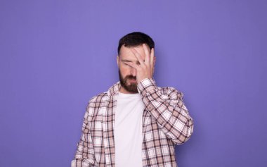 Mor arka planda, sakallı ve günlük giysileri olan genç beyaz bir adam. 