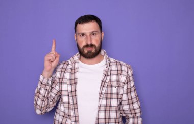 Mor arka planda parmağını gösteren sakallı genç adam, reklam konsepti..     
