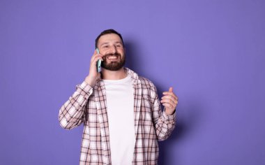 Mor arka planda telefonla konuşan neşeli bir adamın portresi.