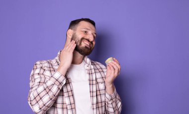 Yakışıklı sakallı adam mor arka planda sakal kremi tutuyor..   