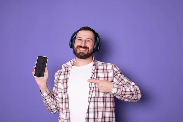 Mor Arka Planda Akıllı Telefon Kullanan Kulaklıklı Gülümseyen Genç Adamın — Stok fotoğraf