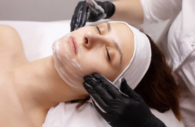 Kozmetoloji prosedürlerinden önce kadın bir müşterinin yüzünü yıkamak ve kurutmak. 