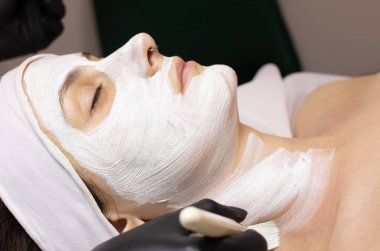 Genç güzel bir kadın güzellik salonunda beyaz yüz maskesi takıyor..   