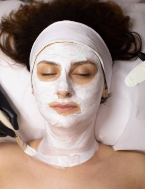 Genç güzel bir kadın güzellik salonunda beyaz yüz maskesi takıyor..   