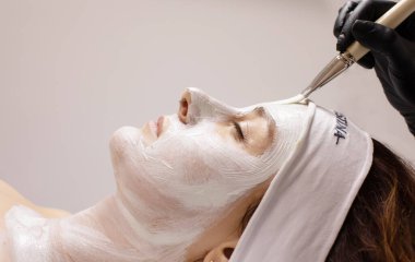 Genç güzel bir kadın güzellik salonunda beyaz yüz maskesi takıyor..   