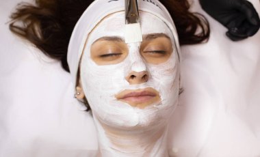 Genç güzel bir kadın güzellik salonunda beyaz yüz maskesi takıyor..   