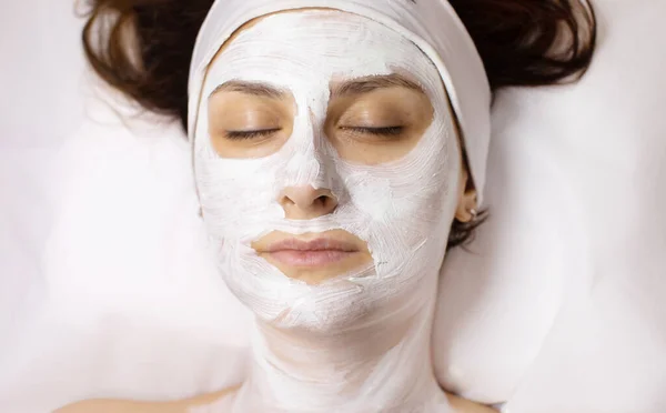 Face mask, spa beauty treatment. Woman applying facial clay mask at spa salon, skincare.