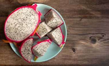 Dilimlenmiş ejderha meyvesinin yakın plan görüntüsü, ahşap masa arkasında tabakta egzotik ejderha meyvesi. Pitahaya.      