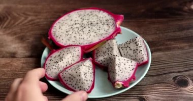 Dilimlenmiş ejderha meyvesinin yakın plan görüntüsü, ahşap masa arkasında tabakta egzotik ejderha meyvesi. Pitahaya.      