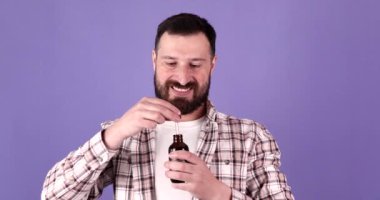 Yakışıklı sakallı adam elinde pippete, mor arka planda sakal yağı var.. 