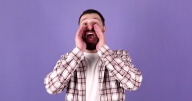 Yanıma gel! Neşeli, dost canlısı, yakışıklı, sakallı bir adam yaklaşıyor ve mor arka planda kameraya gülümsüyor.