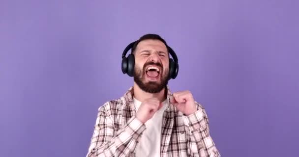 Емоційний Бородатий Чоловік Слухає Музику Навушниках Фіолетовому Фоні Танцює Співає — стокове відео