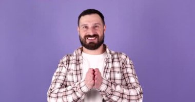 Genç beyaz sakallı yakışıklı adam elleriyle bir şey tutuyor, bir ürün gösteriyor, gülümsüyor ve mutlu bir şekilde izole edilmiş mor arka planda..