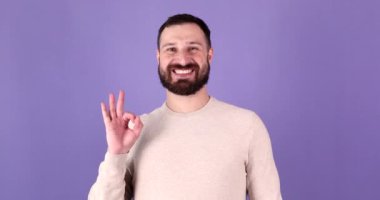 Genç sakallı adam el işaretini onaylar gibi gösteriyor. Milenyum çocuğu tamamen kabul ediyor ve destekliyor. Mor stüdyo arka planında izole edilmiş..