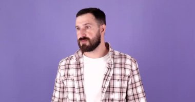 Mor arka planda poz veren korkunç duygusal sakallı genç adam.