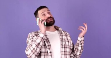 Mutlu gülümseyen sakallı bir adamın portresi mor arka planda izole bir şekilde cep telefonuyla konuşuyor..