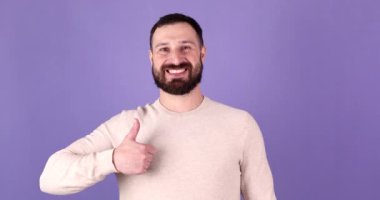 Mor arka planda gülümseyen sakallı adamın portresi. Adam iyi niyet gösterisi yapıyor..