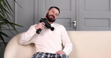 Evinde masaj cihazıyla vücuduna masaj yapan bir adam..