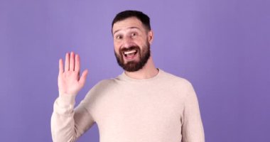 Yakışıklı, gülümseyen sakallı bir adam el sallıyor. Mor arka plan stüdyo resminde izole edilmiş birini görünce el ele tutuşuyor..