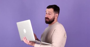 Bilgisayarı kullanarak görüntülü görüşme yapan sakallı adam. Mor arka plan üzerinde çalışan bilgisayarla konuşan yakışıklı bir adam.
