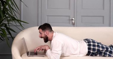 Genç sakallı adam evdeki kanepede uzanmış video görüşmesi yapıyor.