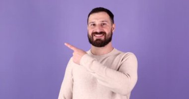 Yakışıklı sakallı, stil sahibi, kendine güvenen, mor arka planda boş fotokopi alanını işaret eden adam.                    