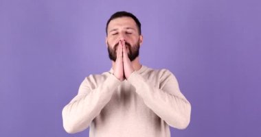 Mor arka planda izole edilmiş genç sakallı beyaz adam dua etmek için el ele tutuşuyor.     
