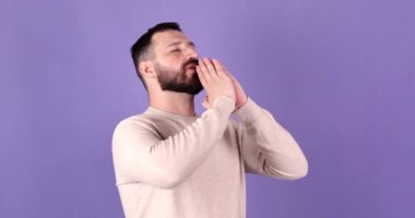 Mor arka planda izole edilmiş genç sakallı beyaz adam dua etmek için el ele tutuşuyor.     