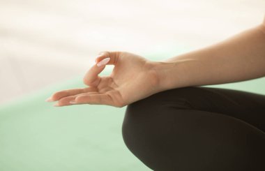 Yoga yapan genç bir kadın, sağlıklı yaşam tarzı ve refah kavramı. Yarım Lotus Mudra hareketi ile poz veriyor, spor yapıyor, kapalı mekanda yakın plan.    