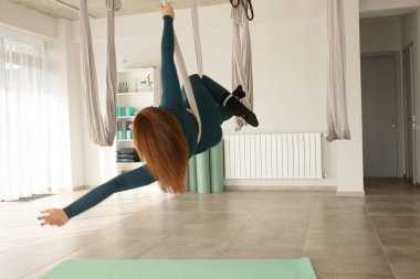 Havadan ya da uçaktan yoga pozu veren genç bir kadın. Sportif kadın uçuş yoga eğitimi alıyor ve fitness stüdyosunda geriniyor, fotokopi odası. Sağlık, spor, yoga konsepti.    