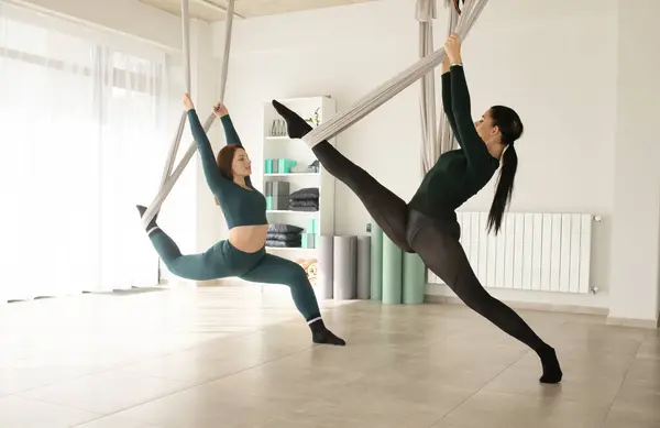 Two women working out with straps during fly yoga. Aero yoga class.
