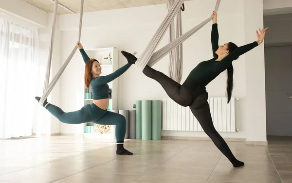 Two women working out with straps during fly yoga. Aero yoga class.