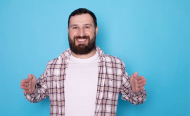 Mavi arka planda izole edilmiş, gülümseyen sakallı genç bir adamın portresi..