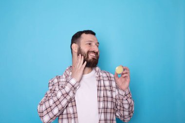 Yakışıklı sakallı adam mavi arka planda sakal kremi tutuyor..