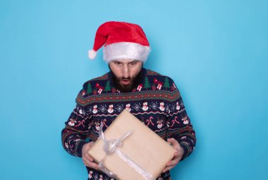 Mavi arka planda hediye kutusu olan, Noel Baba şapkalı çekici sakallı adam. Noel ya da Yeni Yıl konsepti.    