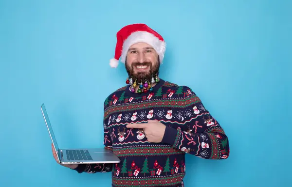 带着愉快胡子的男人 留着装饰过的圣诞胡子 指着笔记本电脑 蓝色背景 — 图库照片
