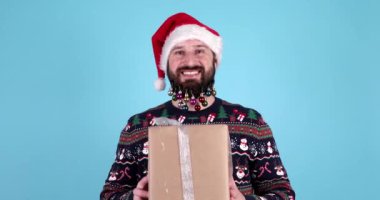 Mavi arka planda hediye kutusu olan, Noel Baba şapkalı çekici sakallı adam. Noel ya da Yeni Yıl konsepti.    