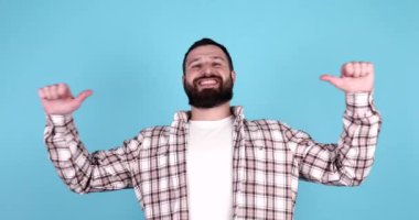 Mavi arka planı gösteren sıradan giysili, gülümseyen, sakallı, genç, çekici bir adam.. 