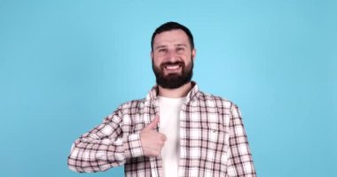 Mavi arka planda izole edilmiş, gülümseyen sakallı genç bir adamın portresi..