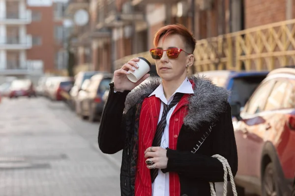 Göz kamaştırıcı bir kadının açık hava moda portresi. Orta yaşlı kadın kahve içiyor ve caddede yürüyor..  