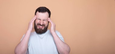 Mutsuz, üzgün bir adam şakaklarına masaj yapıyor. Bej arka planda stüdyoda korkunç bir acıyı dindirmeye çalışıyor..